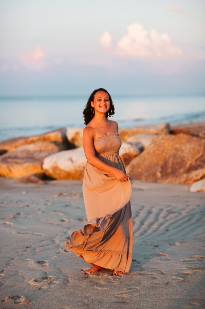 Editorial senior portrait of a high school senior twirling along the shoreline in a beige maxi dress during a beach senior photography session in Cape Cod, Massachusetts with Jennifer Helmka, Photographer.