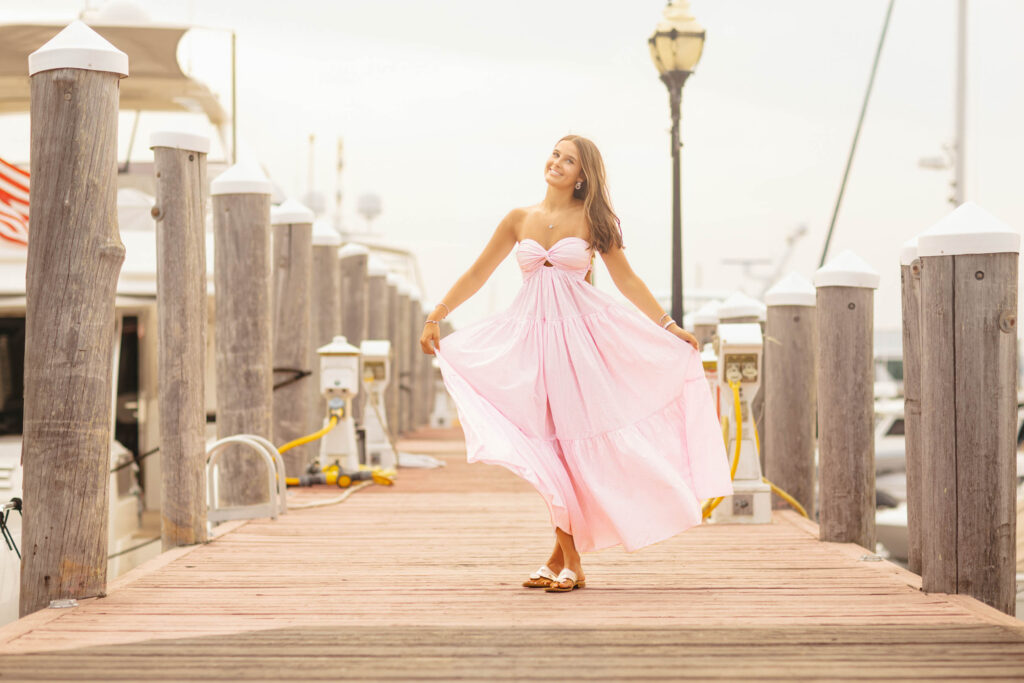 Editorial senior portrait of a high school senior twirling in a pink maxi dress on a marina dock during a senior photography session in Newport, Rhode Island with Jennifer Helmka, Photographer.