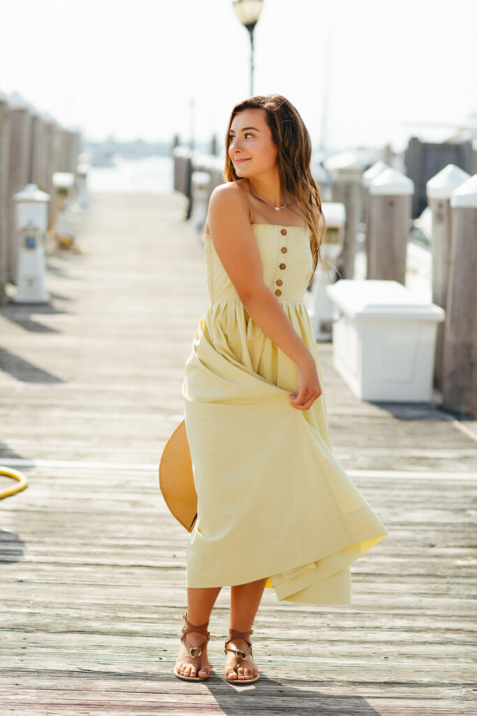 Editorial senior portrait of a high school senior wearing a pale yellow maxi dress on a marina dock during a senior photography session in Newport, Rhode Island with Jennifer Helmka, Photographer.